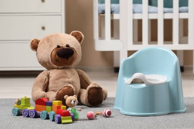Açık mavi bebek lazımlığı ve odada halı üzerinde oyuncaklar. Tuvalet eğitimi