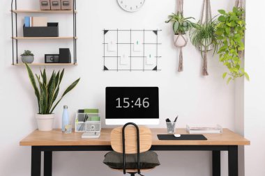Bilgisayarlı, modern mobilyalı ve evdeki ev bitkileriyle rahat bir iş yeri.