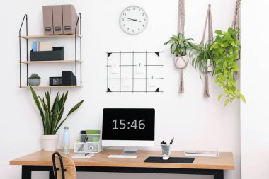 Bilgisayarlı, modern mobilyalı ve evdeki ev bitkileriyle rahat bir iş yeri.