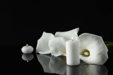 Beyaz zambak çiçekleri ve siyah ayna yüzeyinde yanan mumlar karanlıkta, yazı için boşluk. Cenaze sembolleri