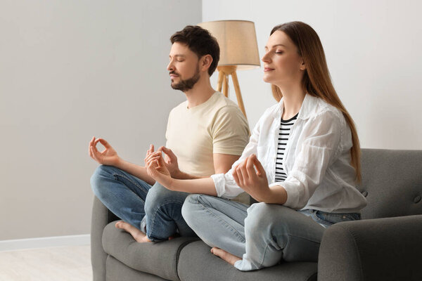 Couple meditating together on sofa at home. Harmony and zen