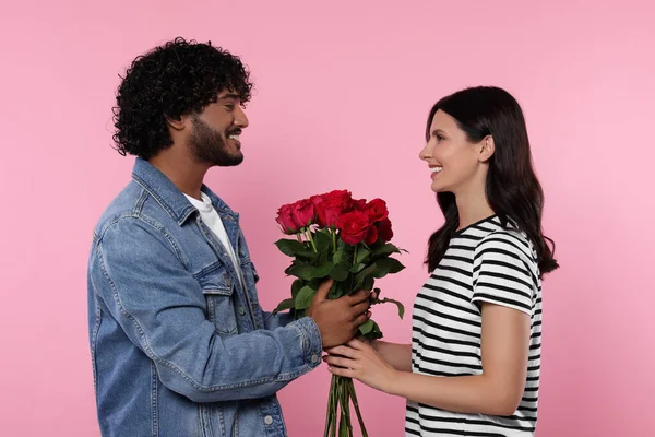 International dating. Happy couple with bouquet of roses on pink background