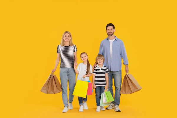 家庭购物 快乐的父母和孩子们 他们带着许多色彩艳丽的购物袋 背景为橙色 — 图库照片