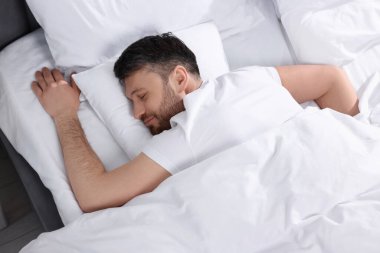 Yumuşak yatakta uyuyan yakışıklı adam, üst manzara.