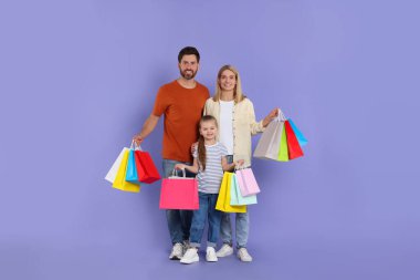 Aile alışverişi. Mor arka planda renkli çantaları olan mutlu anne ve baba ve kız.