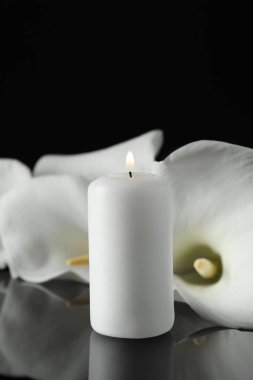 Karanlıkta siyah ayna yüzeyinde yanan mum ve beyaz zambak çiçekleri, metin için yeri olan yakın plan. Cenaze sembolü