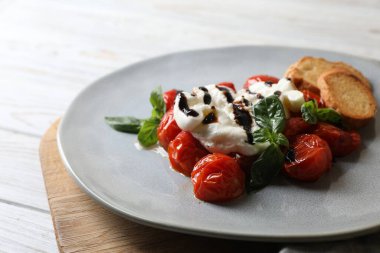 Beyaz ahşap masada domates, kızarmış ekmek ve fesleğen sosuyla servis edilen nefis burrata peyniri.