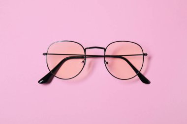 Pembe arka planda siyah çerçeveli gözlüklü şık bir çift gözlük.
