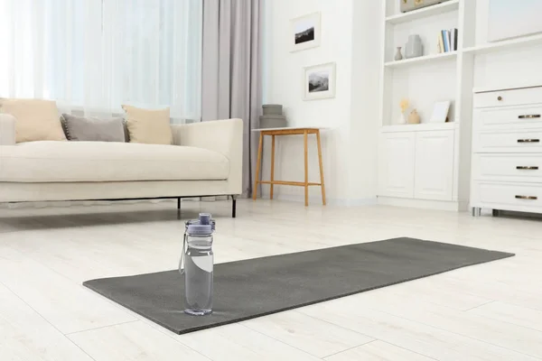 Yoga mat and bottle of water on floor in room