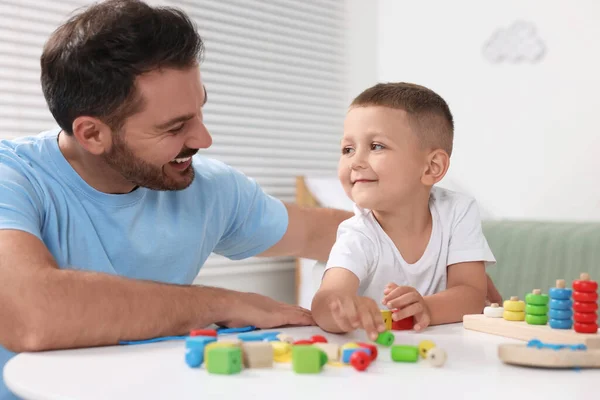 Motor skills development. Father and his son playing with colorful wooden pieces at table indoors