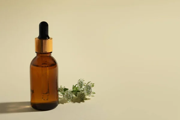 Bottle with cosmetic oil and flower on beige background, space for text