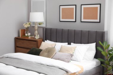 Yastıkları, lambası ve odasındaki ahşap çekmecelerde farklı dekorları olan rahat bir yatak. Şık iç mekan