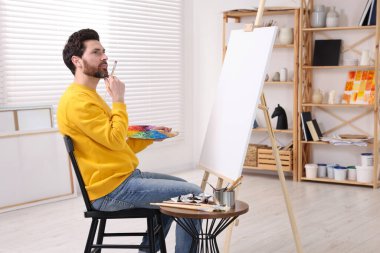 Stüdyoda resim yapan adam. Tuvali tutmak için resim sehpası kullanılıyor