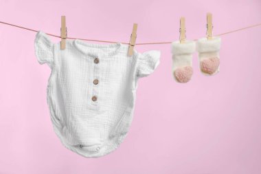 Güzel bebek tulumu ve çorapları pembe arka planda çamaşır ipinde kuruyor.