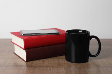 Siyah seramik bardak, bir yığın kitap ve ahşap masada akıllı telefon.