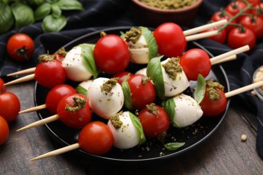 Domatesli şişler, mozarella topları, fesleğen ve pesto sosu ahşap masada, yakın plan.