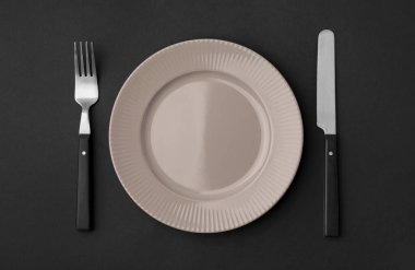 Siyah arka planda çatal bıçak takımı olan temiz bir tabak.