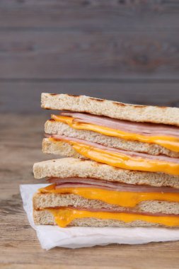 Ahşap masada jambon ve peynirli leziz ızgara sandviçler, yakın plan.