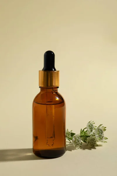 Bottle with cosmetic oil and flower on beige background