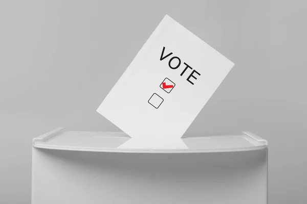 Paper with word Vote and tick sticking out of ballot box on light grey background