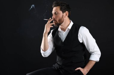 Siyah arka planda sigara içmek için sigara tutacağı, metin için boşluk kullanan adam
