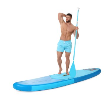 Beyaz arka plana karşı mavi SUP panosunda kürek çeken yakışıklı bir adam.