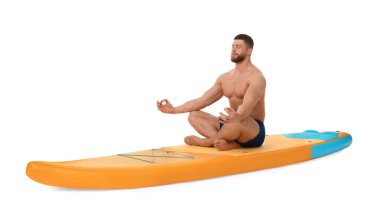 Beyaz arka planda turuncu SUP tahtasında yoga yapan yakışıklı bir adam.