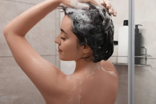 Beautiful woman washing hair with shampoo in shower, back view