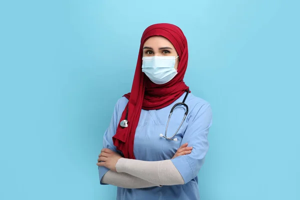 身穿头巾 医疗制服和浅蓝色背景防护面具的穆斯林妇女 — 图库照片