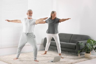 Üst düzey çift evde dizüstü bilgisayarla yoga yapıyor.