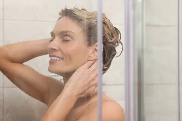 快乐的女人在淋浴间里洗头 透过玻璃看 — 图库照片