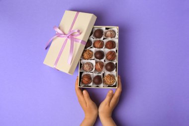Açık mor arka planda bir kutu lezzetli çikolata şekeri olan çocuk, üst görünüm