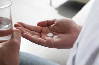 Bulanık arka planda bir bardak su ve hap olan adam, yakın plan.