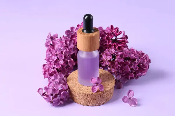 Bottle with essential oil and lilac flowers on violet background