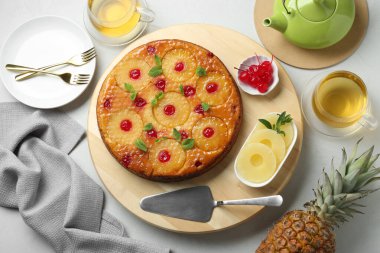 Beyaz masa üzerinde çay ve malzemelerle servis edilen nefis ananaslı kek.