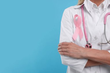 Açık mavi arka planda pembe kurdeleli ve steteskoplu bir doktor, yakın plan ve metin için boşluk. Göğüs kanseri farkındalığı