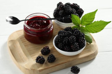 Taze böğürtlen, lezzetli reçel ve beyaz ahşap masada yapraklar.