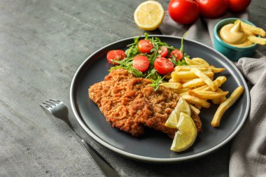 Patates kızartması, domates ve roka ile servis edilen lezzetli şnitzeller gri masada, yakın plan.