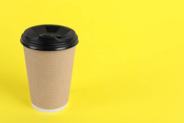 Sarı arka planda plastik kapaklı kağıt bardak, metin için boşluk. Kahve hazır.