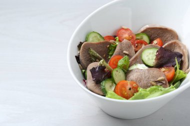 Biftek diliyle nefis bir salata ve beyaz ahşap masada sebzeler, yakın plan. Metin için boşluk