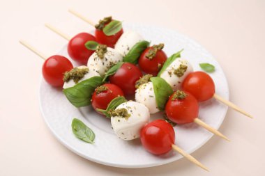 Domatesli şişler, mozarella topları, bej arka planda fesleğen ve pesto sosu, yakın plan.