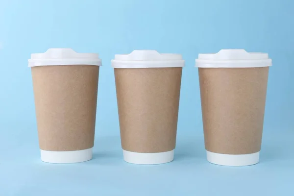 Paper cups with white lids on light blue background. Coffee to go