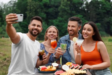 Kokteyl kadehleriyle dışarıda selfie çeken mutlu arkadaşlar.