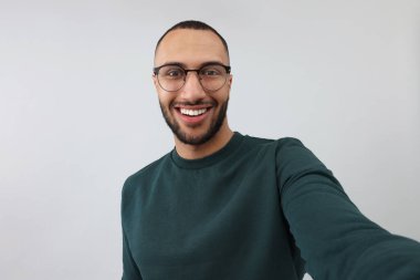 Gülümseyen genç adam gri arka planda selfie çekiyor.