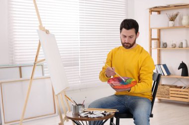 Stüdyoda resim yapan adam. Tuvali tutmak için resim sehpası kullanılıyor