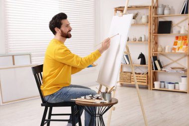 Stüdyoda resim yapan adam. Tuvali tutmak için resim sehpası kullanılıyor