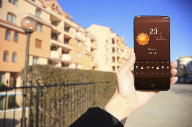 Güneşli bir günde açık hava telefonunda hava durumu uygulaması kullanan bir adam, yakın plan. Veri, güneş ve diğer illüstrasyonlar ekranda
