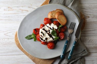 Beyaz ahşap masada domates, kızarmış ekmek ve fesleğen sosuyla servis edilen nefis burrata peyniri.