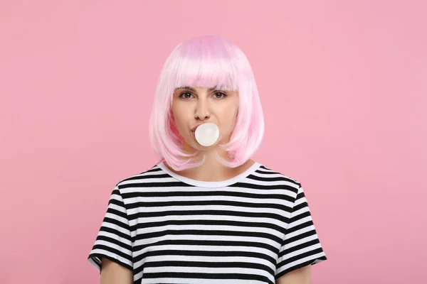 Beautiful woman blowing bubble gum on pink background