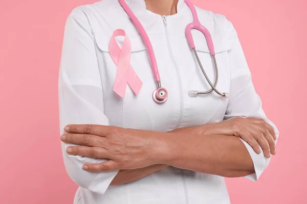 Doctor with pink ribbon and stethoscope on color background, closeup. Breast cancer awareness